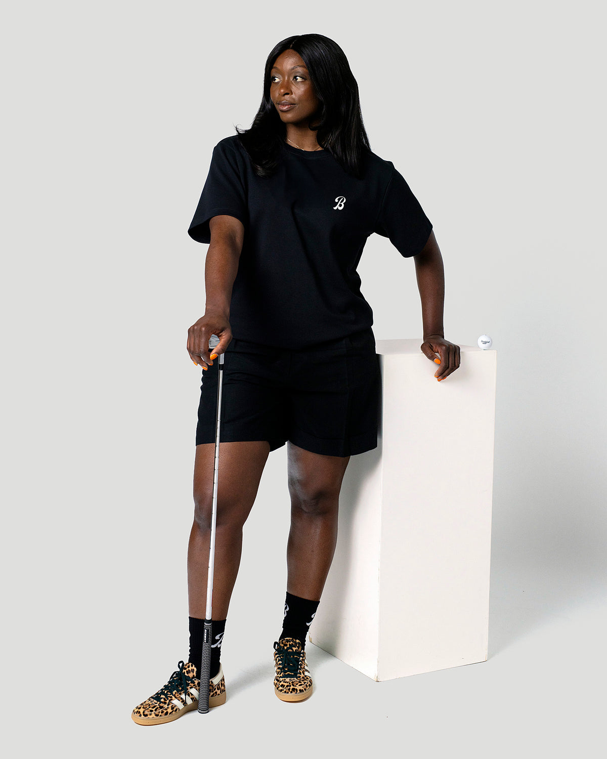 Woman in the black Gus Gus Tee standing side-on with a golf club