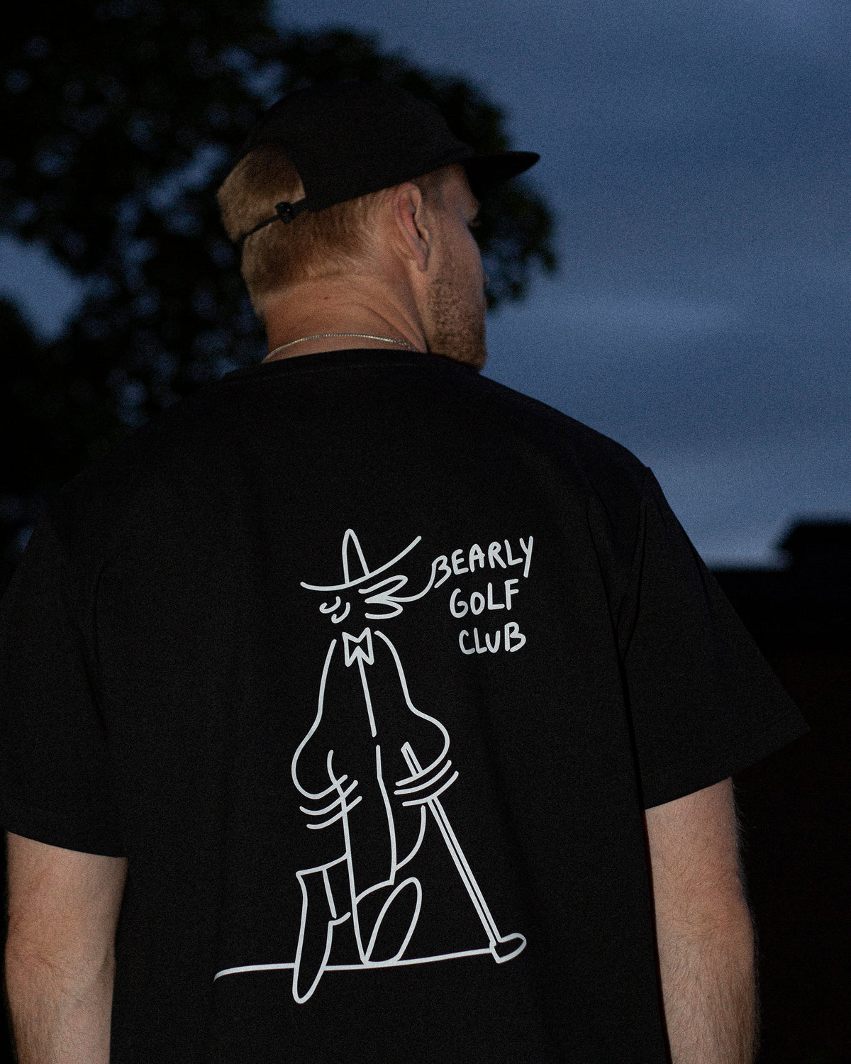 Close-up at dusk of a man from behind wearing the tee, Gus Gus artwork visible on the back