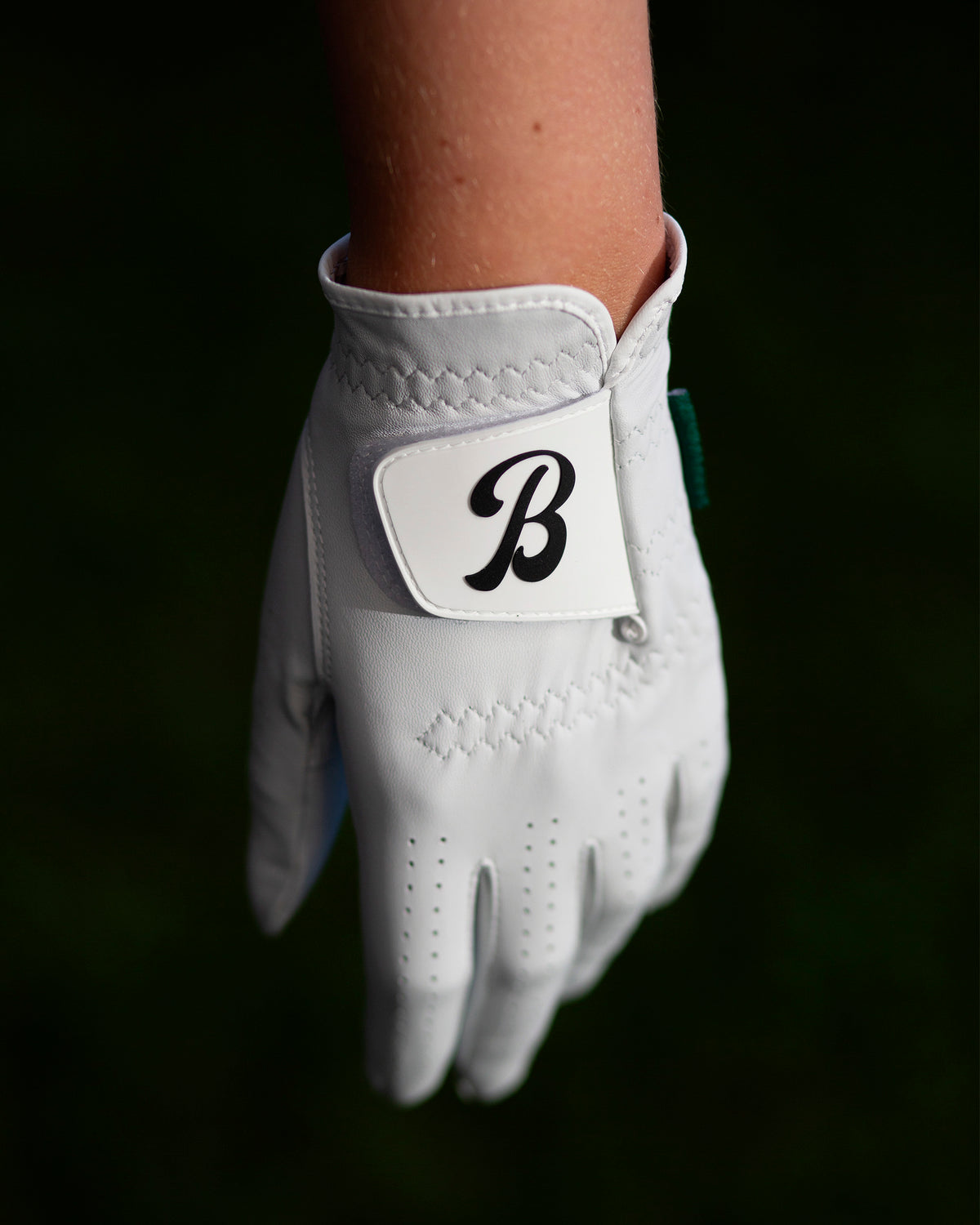 Close-up of a wrist wearing the glove, showing the strap closure and "B" logo patch