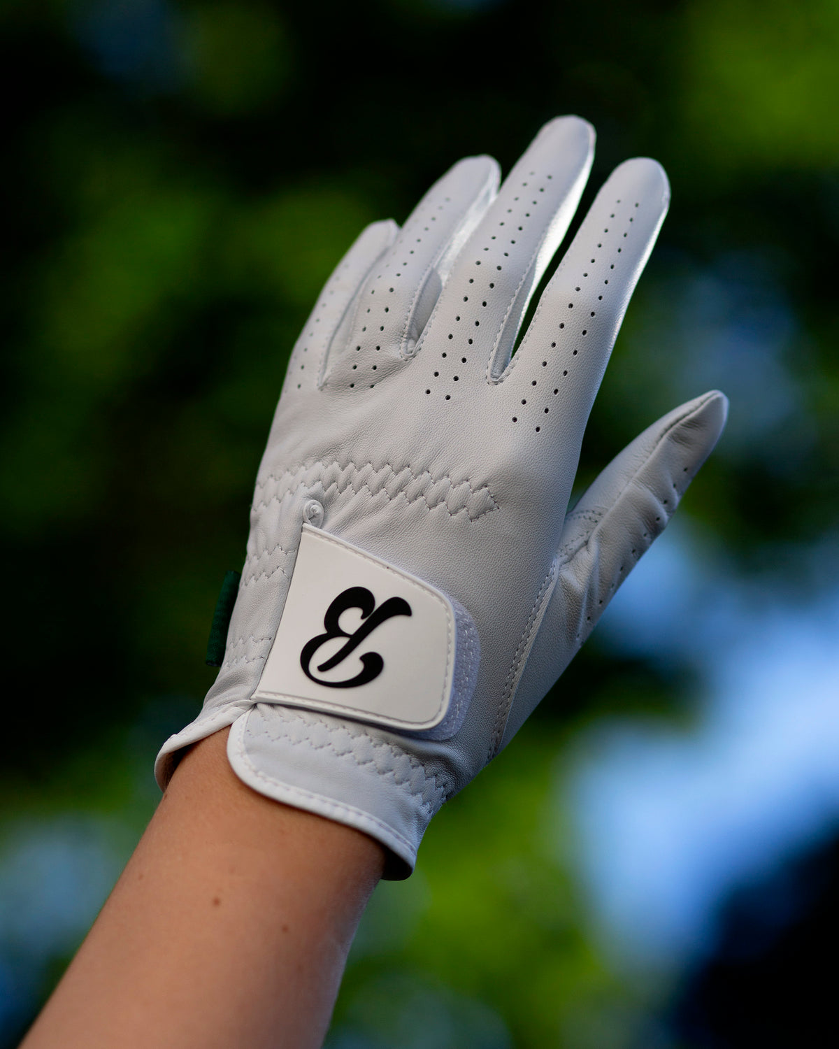 Hand and wrist wearing the glove, showing perforated finger detailing and the wrist-strap logo patch